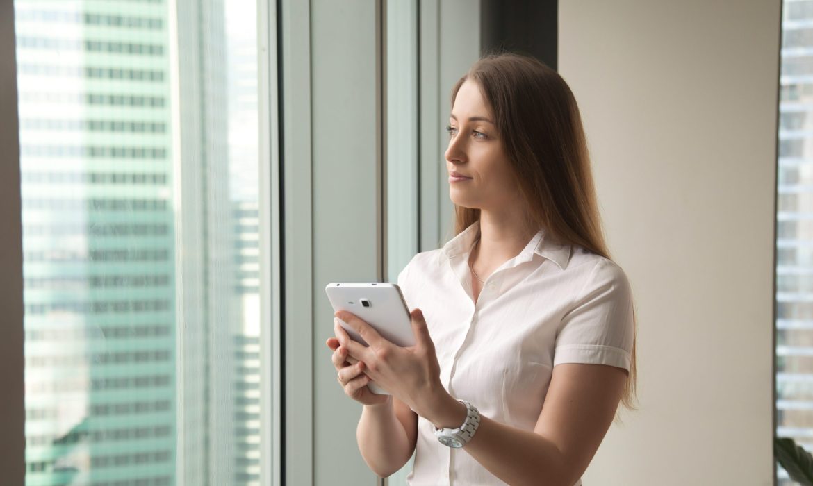 Young dreamy beautiful businesswoman looking through window whil