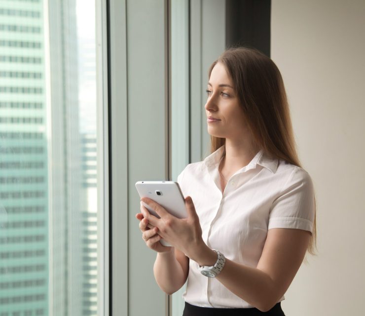 Young dreamy beautiful businesswoman looking through window whil